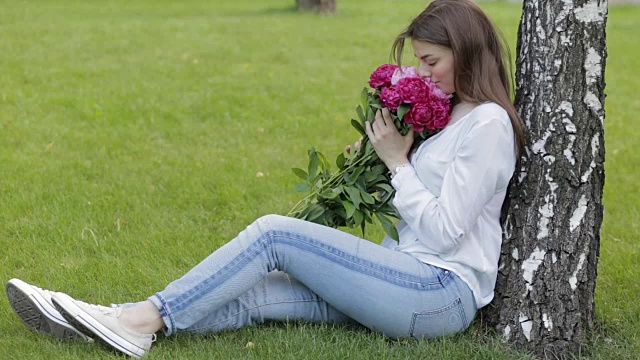 女人坐在公园的草地上，捧着牡丹花视频素材