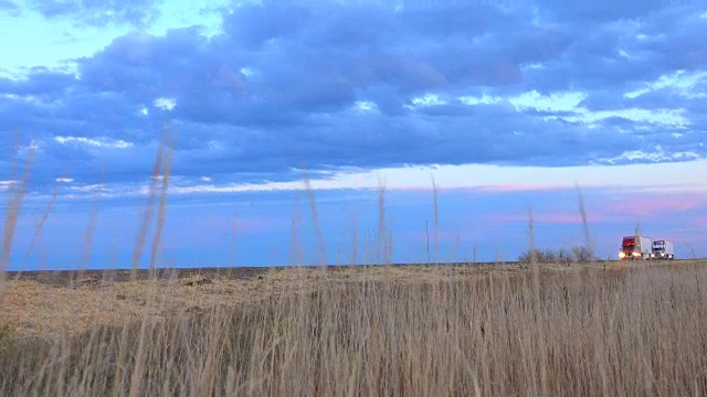 特写:两辆卡车在日出时行驶在空旷的荒野公路上视频素材