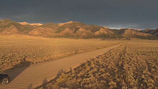 空中黑色越野车驾驶在尘土飞扬的道路上走向雄伟的落基山脉视频素材