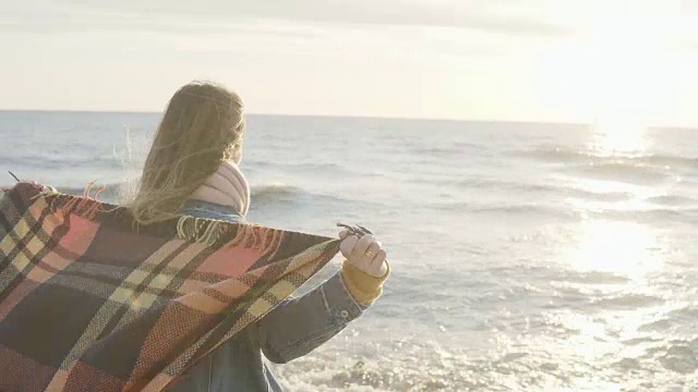 自由:年轻女子站在海边，手举格子。快乐的女性在寒冷的刮风的一天在海滩上视频素材