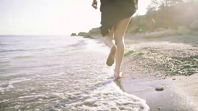 漂亮的微笑的女孩跑在卵石的海滩附近的海水视频素材