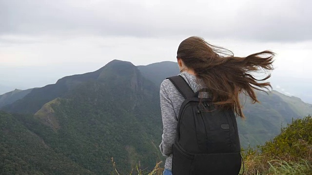 年轻的女游客背包欣赏美丽的风景在山。女游客站在美丽的峡谷边缘，欣赏大自然。慢动作特写后视图视频素材