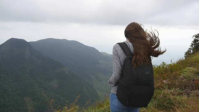 年轻的女游客背包欣赏美丽的风景在山。女游客站在美丽的峡谷边缘，欣赏大自然。慢镜头视频素材