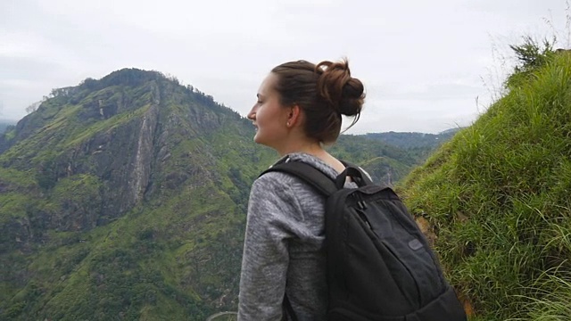 年轻的女游客背包欣赏美丽的风景在山。女游客站在美丽的峡谷边缘，欣赏大自然。慢镜头视频素材