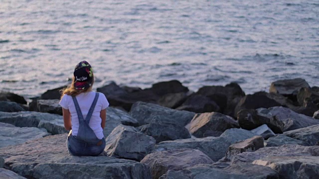 年轻女子坐在那里，看着夕阳，看着大海视频素材