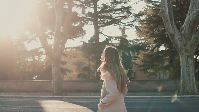 迷人的年轻女子走在公园附近的路在日落。女性享受着明媚的春日，探索着城市视频素材