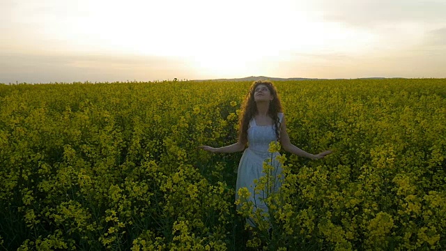 身着白色连衣裙的乡村女孩在夕阳下在一片油菜花田里纺纱视频素材