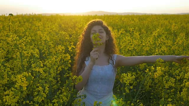 慢镜头里的年轻女子穿着白衣在满是油菜花的田野里翩翩起舞，散发着大自然的气息视频素材