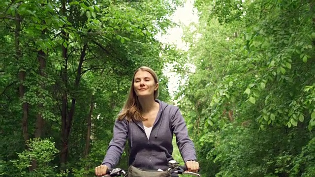 慢动作快乐活跃的运动的年轻女子在夏天的一天骑自行车通过阳光明媚的公园视频素材