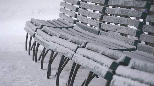 雪花飘落，公园的人行道上有盖着的长凳。慢镜头降雪。冬日公园里寂寞的长椅视频素材