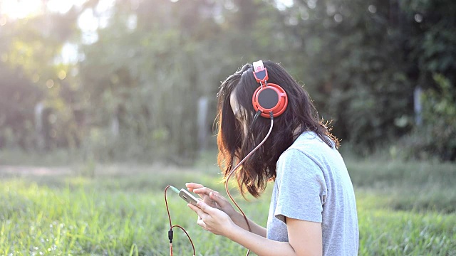 女人喜欢在日落时分用耳机在户外听音乐视频素材