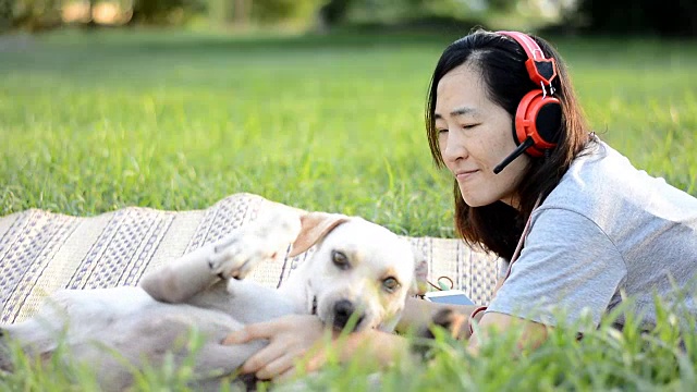 女人喜欢戴着耳机在户外听音乐，和友好的狗玩耍视频素材