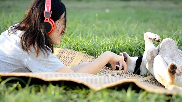 女人喜欢戴着耳机在户外听音乐，和友好的狗玩耍视频素材