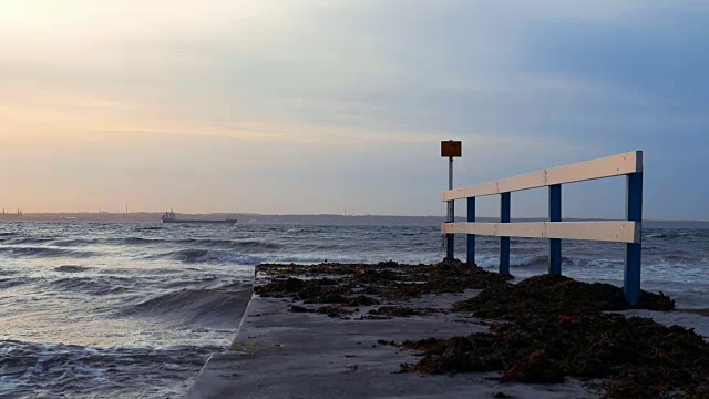 日落时，海浪拍打着码头，远处的货船在背景中慢镜头视频素材