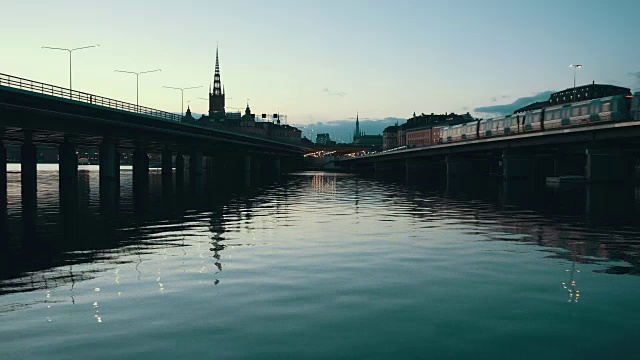 黄昏时分斯德哥尔摩市的桥梁。地铁经过铁路桥。教堂塔楼，城市景观和水渠视频素材