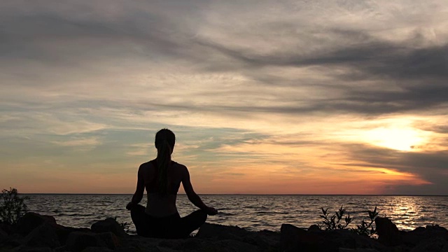 瑜伽女人在莲花姿势在海滩上日落视频素材