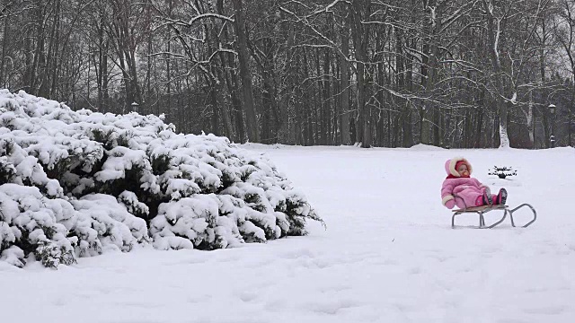 妈妈和小女孩在冬季公园的雪橇上玩得很开心。FullHD视频素材