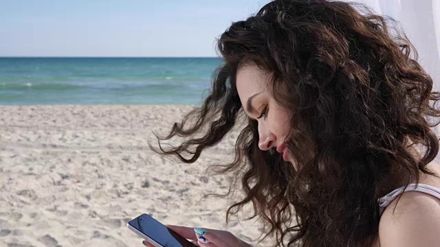 自拍年轻女子在海滩上，手机删除度假照片，微笑的女孩在大海和沙滩上自拍视频素材