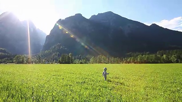 可爱的男孩在草地上，四周是美丽的山景视频素材