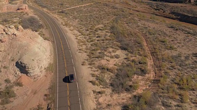 航拍:黑色越野车行驶在峡谷峡谷中蜿蜒的空旷道路上视频素材