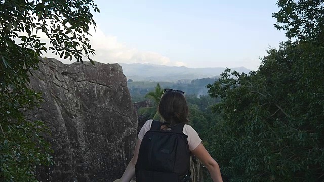 年轻女性徒步旅行者与背包看山。女游客站在美丽的峡谷边缘。慢镜头后视图视频素材