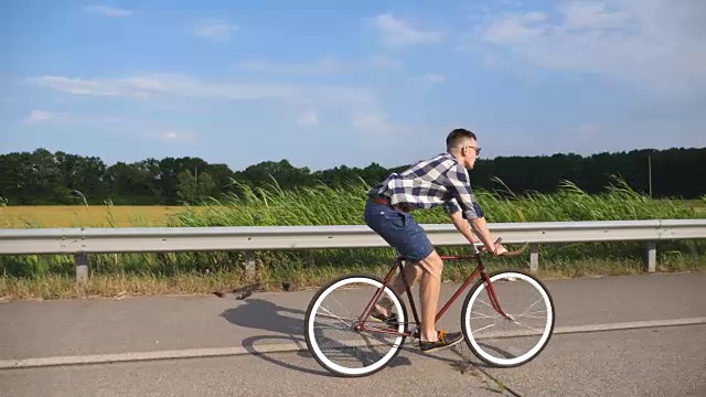 年轻英俊的男子骑着老式自行车在乡间小路上。在赛道上骑自行车的运动员。男性骑自行车者在高速公路上骑固定齿轮自行车。健康积极的生活方式视频素材