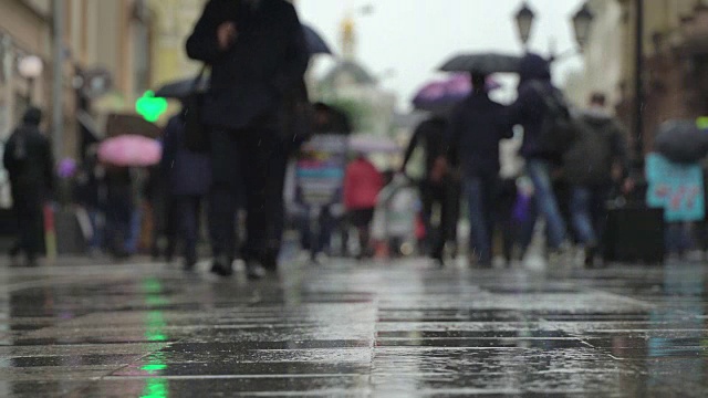 城市街道上的雨天背景。真正的时间。人们在雨中带着雨伞上下班。模糊的散景。自然背景视频素材