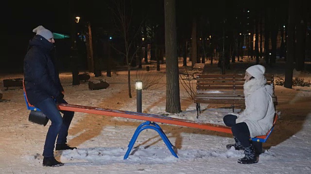 成年男女在冬季的傍晚公园里玩跷跷板视频素材