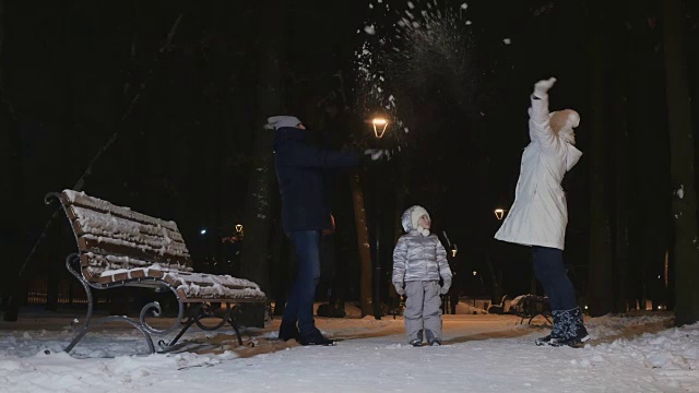 在冬天的傍晚公园里，一对年轻的夫妇把雪扔在小女儿身上视频素材