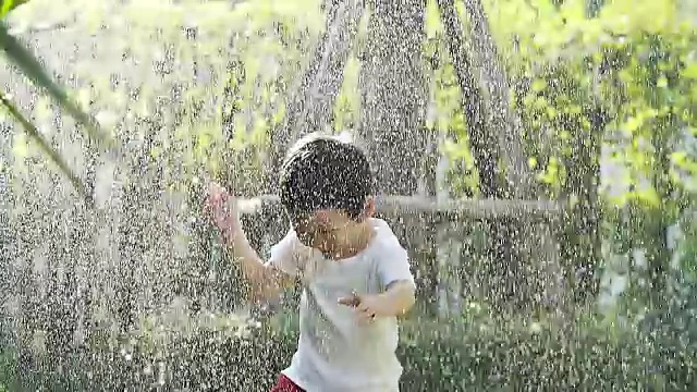 在炎热的夏天，一个小男孩在自家后院的洒水器里玩耍。(慢动作vdo摄像机拍摄)视频素材