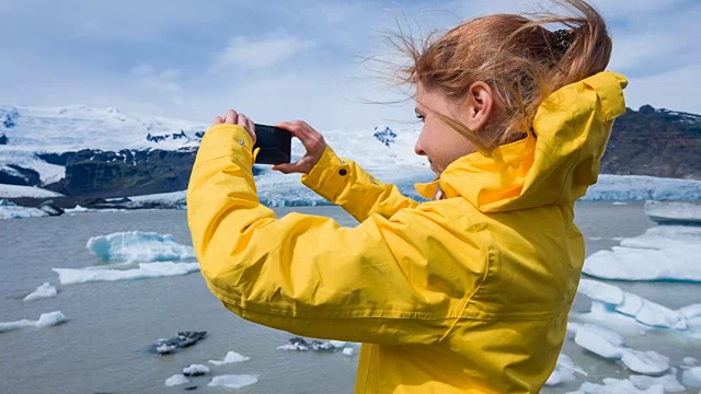 在一个刮风的日子里，一名妇女在Jokulsarlon冰川泻湖拍摄漂浮的冰山视频素材