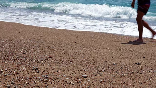 暑假背景是两个年轻人在海滩上散步，海浪在他们身后撞击沙滩上的沙子视频下载