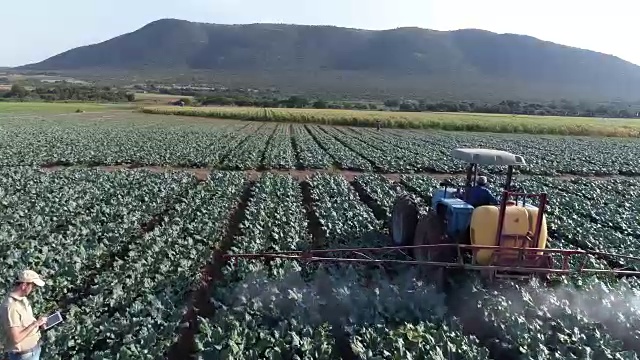 农民使用数字平板电脑的鸟瞰图和监测拖拉机在农作物上喷洒农药视频素材