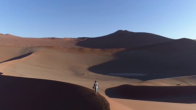 空中平移的男性游客走在纳米布沙漠的一个巨大沙丘的顶部视频素材