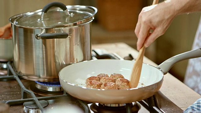 一个烹饪节目中的男厨师正在用木勺检查煎锅里的肉丸视频素材