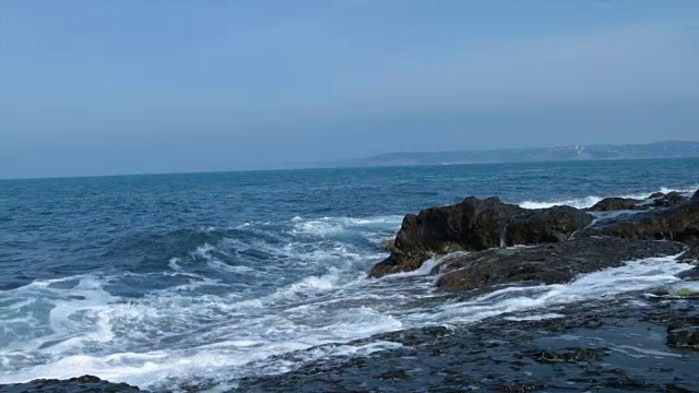 在一个阳光明媚的日子，海浪拍打着岩石视频素材