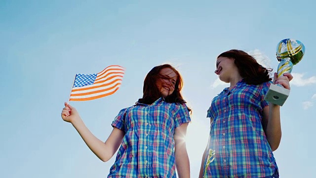 两个十几岁的双胞胎女孩拿着优胜杯和一面美国国旗。冠军，胜利，成就视频素材