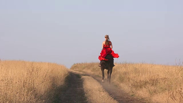 穿着红色长裙的年轻女孩骑着黑马在干燥的草原上视频素材