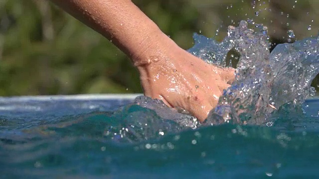 女子的手滑过水面，溅起水池中的水花视频素材