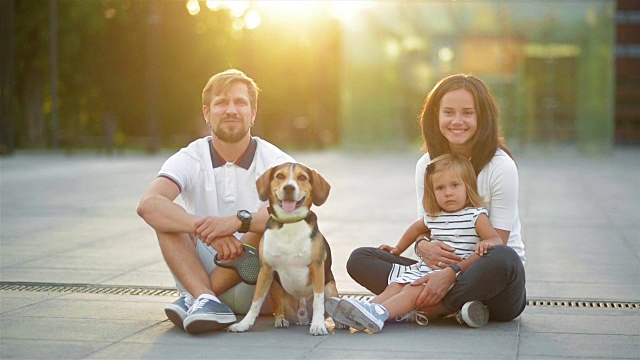 户外肖像的年轻家庭与小女儿和他们的比格犬在城市在夏季日落视频素材