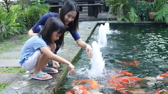 亚洲女孩和母亲在池塘里喂鲤鱼视频素材