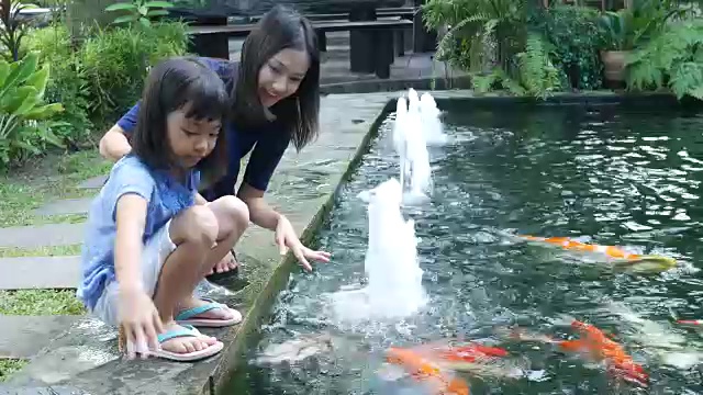 亚洲女孩和母亲在池塘里喂鲤鱼视频素材