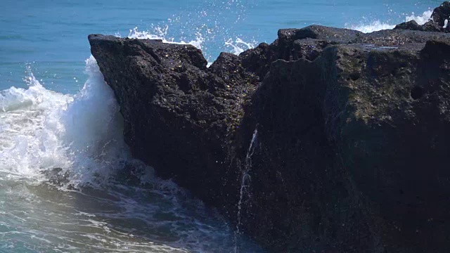 慢动作:海浪撞击黑色的火山岩，溅起水珠视频素材