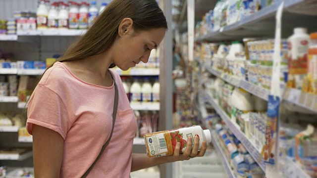 在购物中心的食品杂货店里，一位女士在冰箱里挑选乳制品视频素材