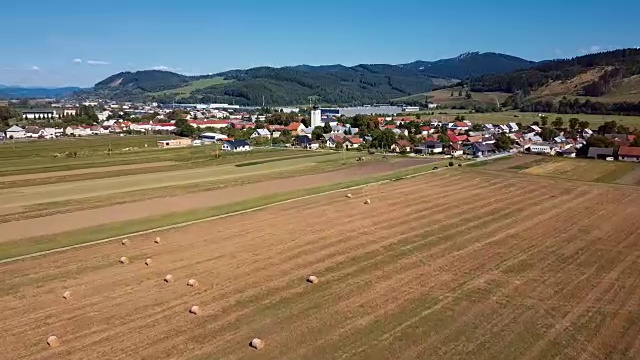 在有圆草堆的田野上空低空飞行。风景如画的小村庄和山峦为背景。视频素材