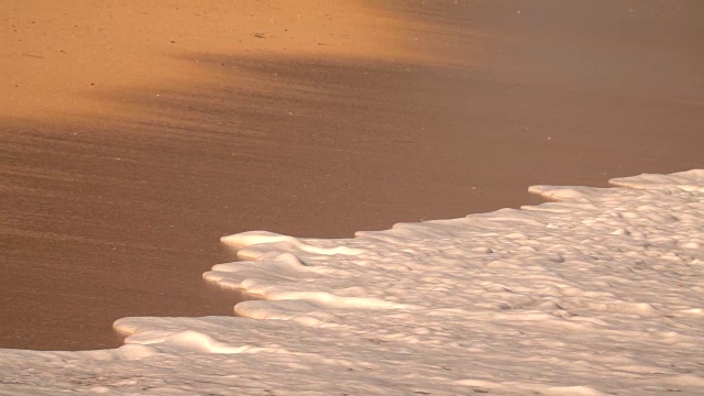 慢镜头:金色的夕阳下，泡沫状的海浪冲刷着橙色的沙滩视频素材