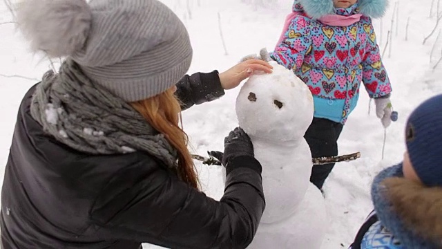 快乐的妈妈和孩子们在公园里堆雪人。视频素材