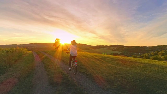 空中SLO MO女子与太阳帽骑在乡村日落视频素材