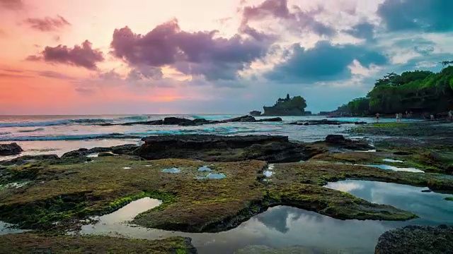 夕阳在破碎的海滩上流逝。在远处，人们可以看到印尼巴厘岛上的塔纳洛特神庙。视频素材