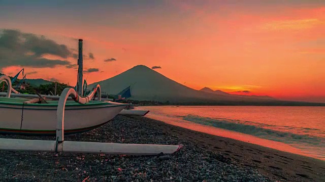 日落俯瞰阿贡火山，背景是一艘渔船在海滩上的阿米德耶梅鲁克湾在印度尼西亚的巴厘岛。视频素材